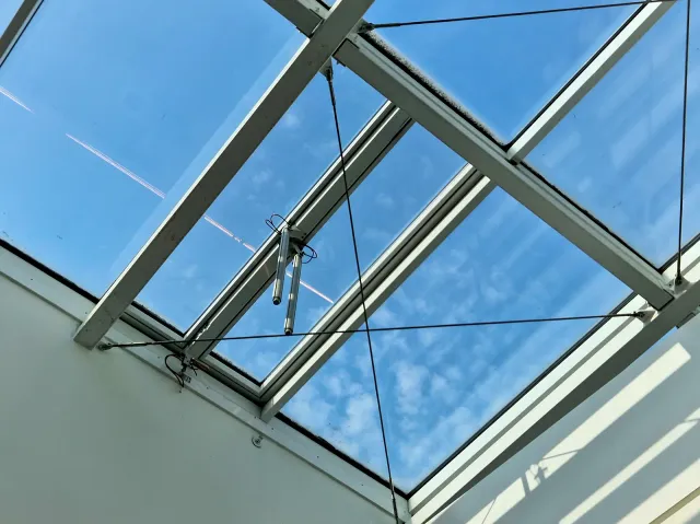 Atrium Skylight with Opening Mechanisms View from below of an atrium skylight with white metal framing, support cables and window opening mechanisms against a blue sky