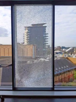 Internal Broken Window Glass Cracked internal window pane in a high-rise building, showing extensive damage across the glass with a city view beyond.