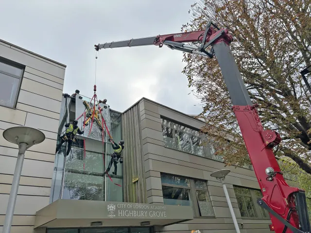 Commercial Glass Replacement at City of London Academy Rope access technicians using a crane-mounted glass lifter to replace a large high-level window panel at City of London Academy Highbury Grove.