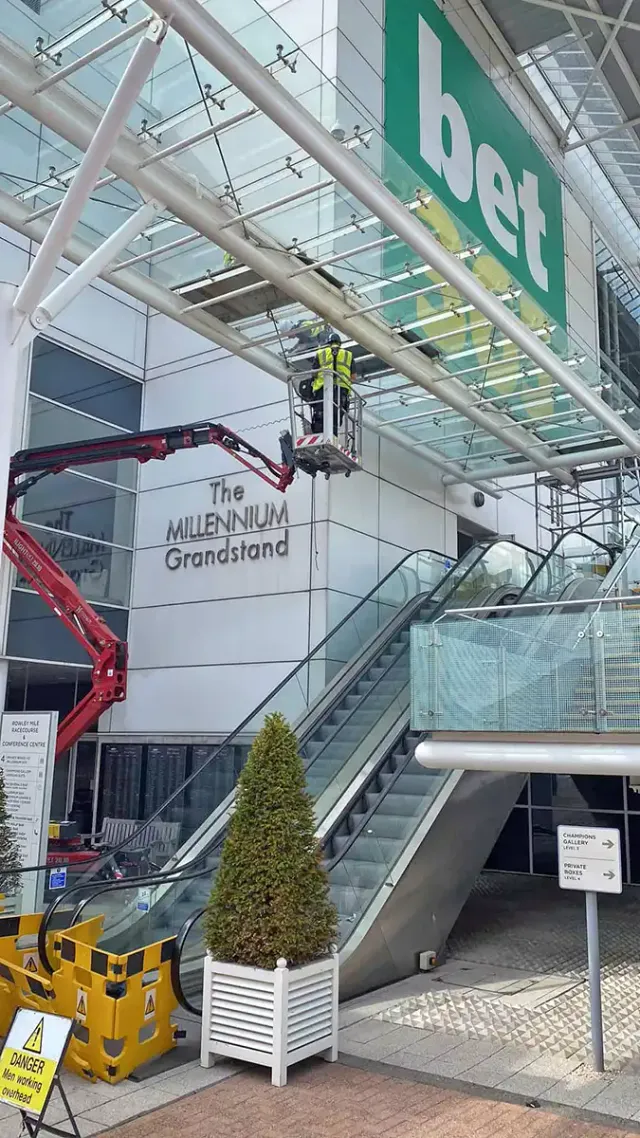 Glass Canopy Repairs at The Millennium Grandstand Technician using a mobile access platform to carry out glass canopy repair work above the entrance to The Millennium Grandstand.