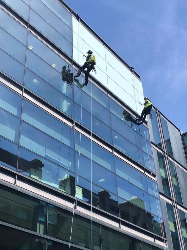 Workmen inspecting glazing using ropes for access