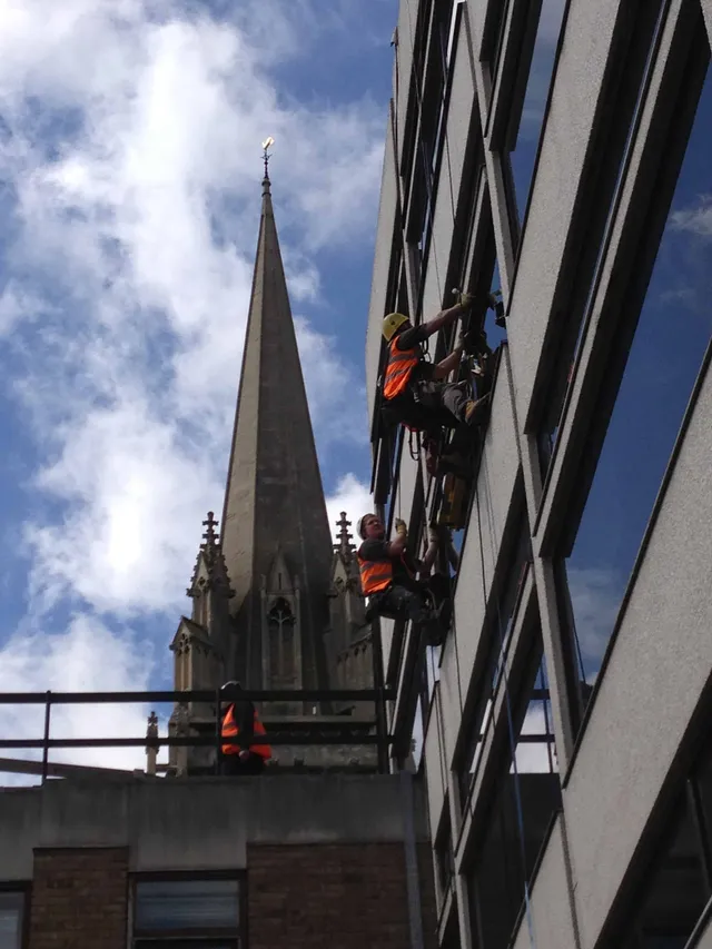 Workmen working on glazing using ropes