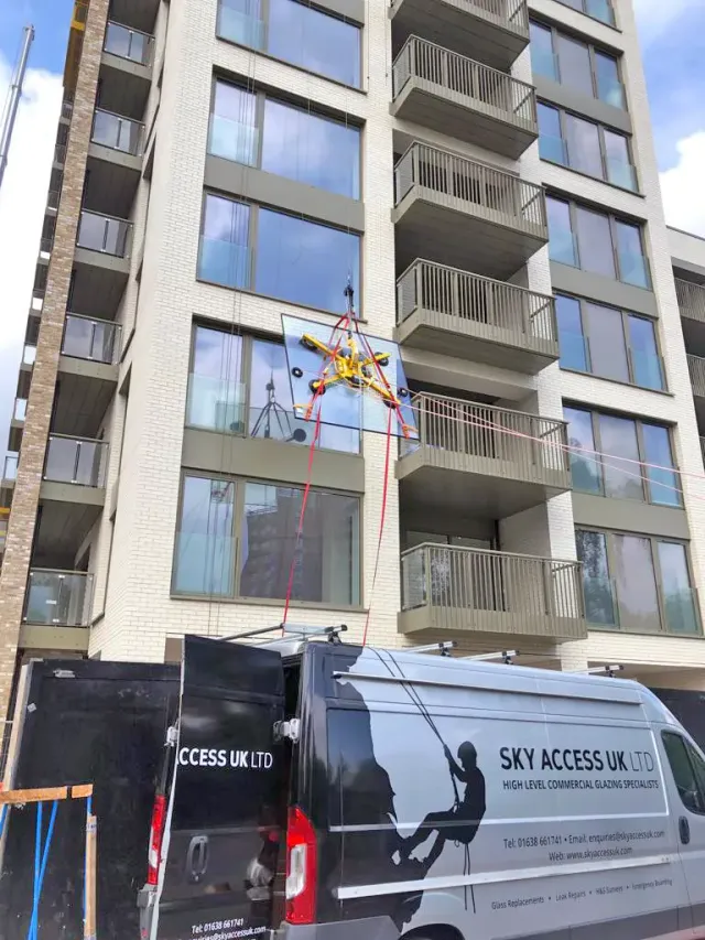 High-Level Glazing Replacement on Commercial Building Sky Access Glazing van parked outside a multi-storey residential building while specialist lifting equipment is used to position a glass panel for high-level glazing work.