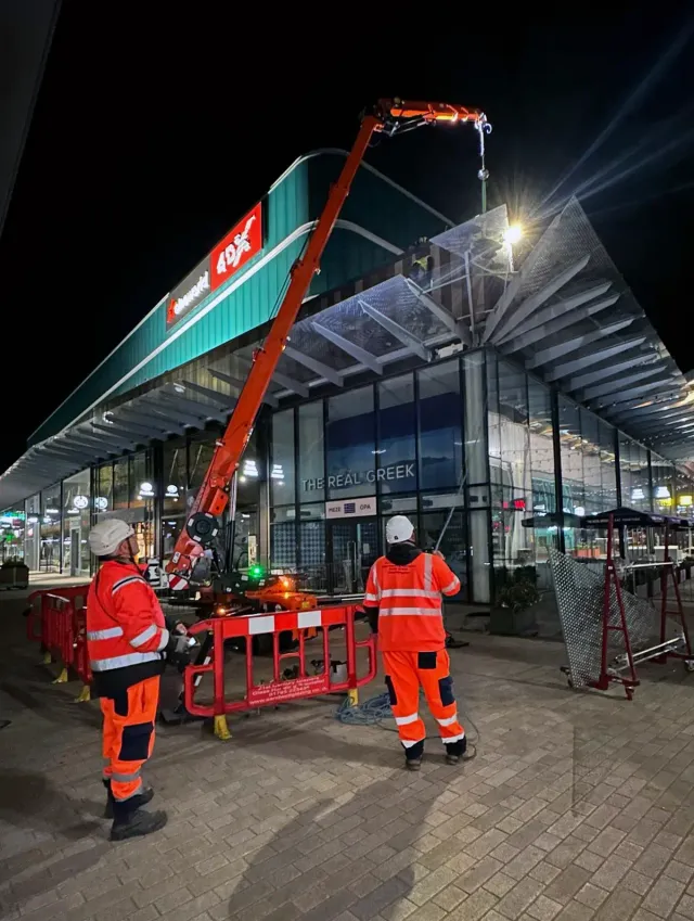 Night-Time Rope Access Installation at Commercial Retail Park Rope access team using a mobile crane to install metal canopy panels on a commercial retail building at night.